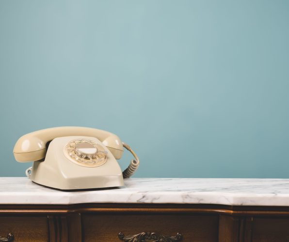 Close-up view of an old telephone on a table with copy space on blue background. Communication and retro style concept.